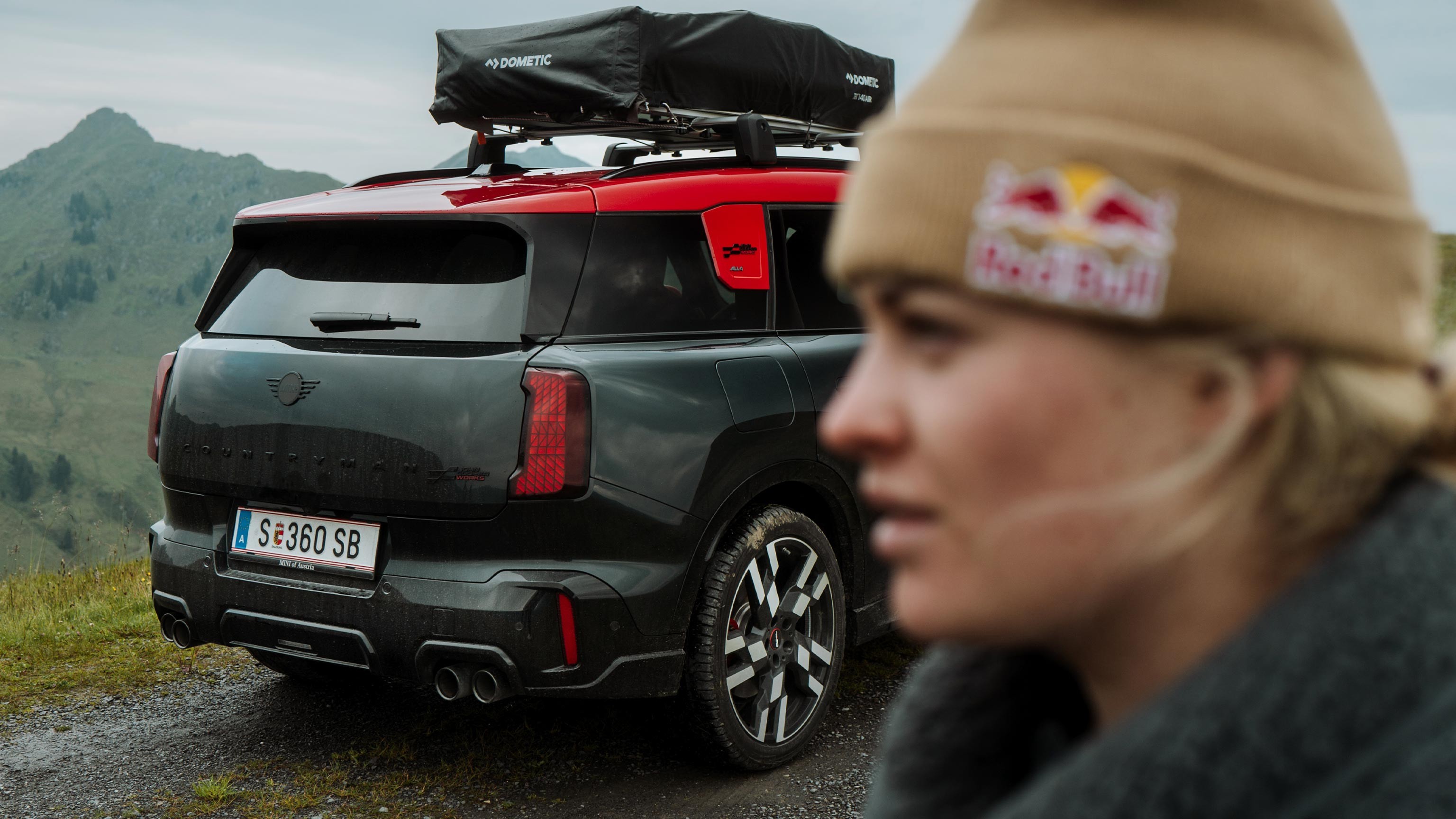 Side profile portrait of Vali Höll and an angled rear view of the new MINI John Cooper Works Countryman ALL4, which we see equipped with a roof rack.
